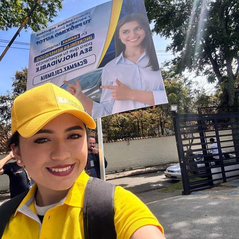 Promotora de AgenciaBTL con gorra y camiseta de marca junto a un aviso de vehículos